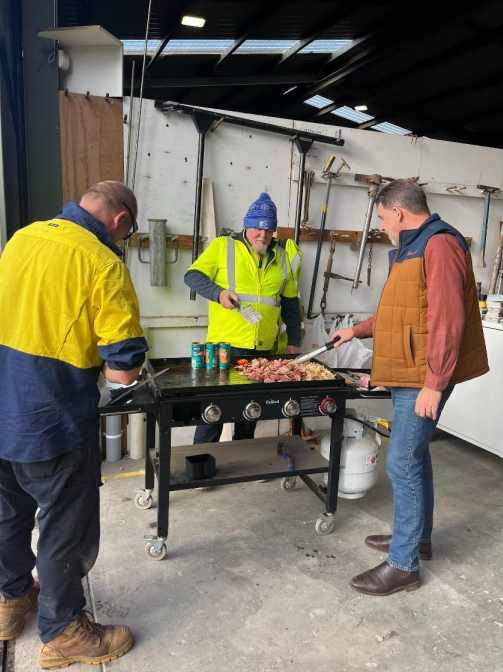 An image of the Mayor Darryl Houston cooking a BBQ with two men from the depot who are wearing florescent shirts