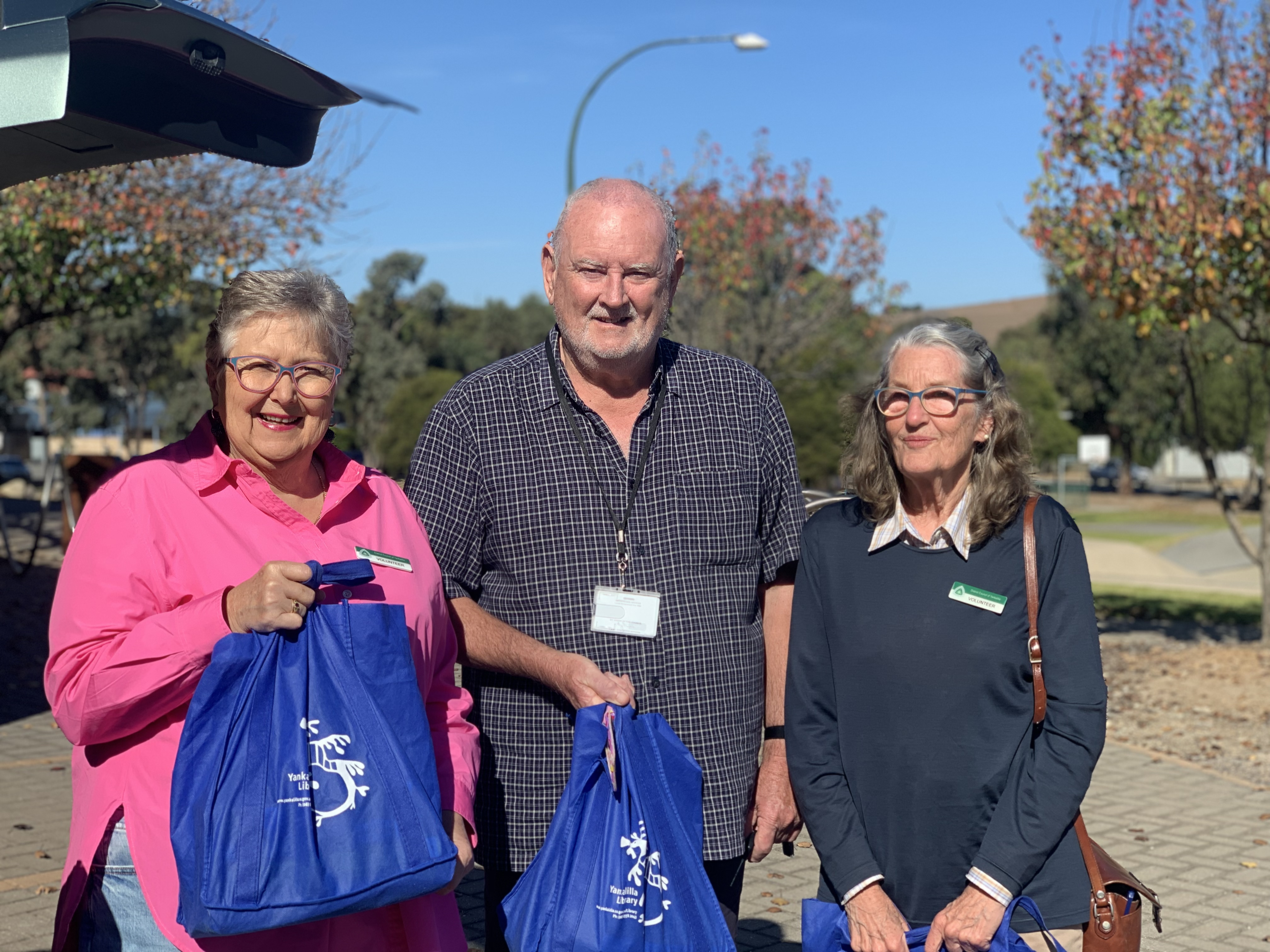 Three people holding library bags and smiling at the camera