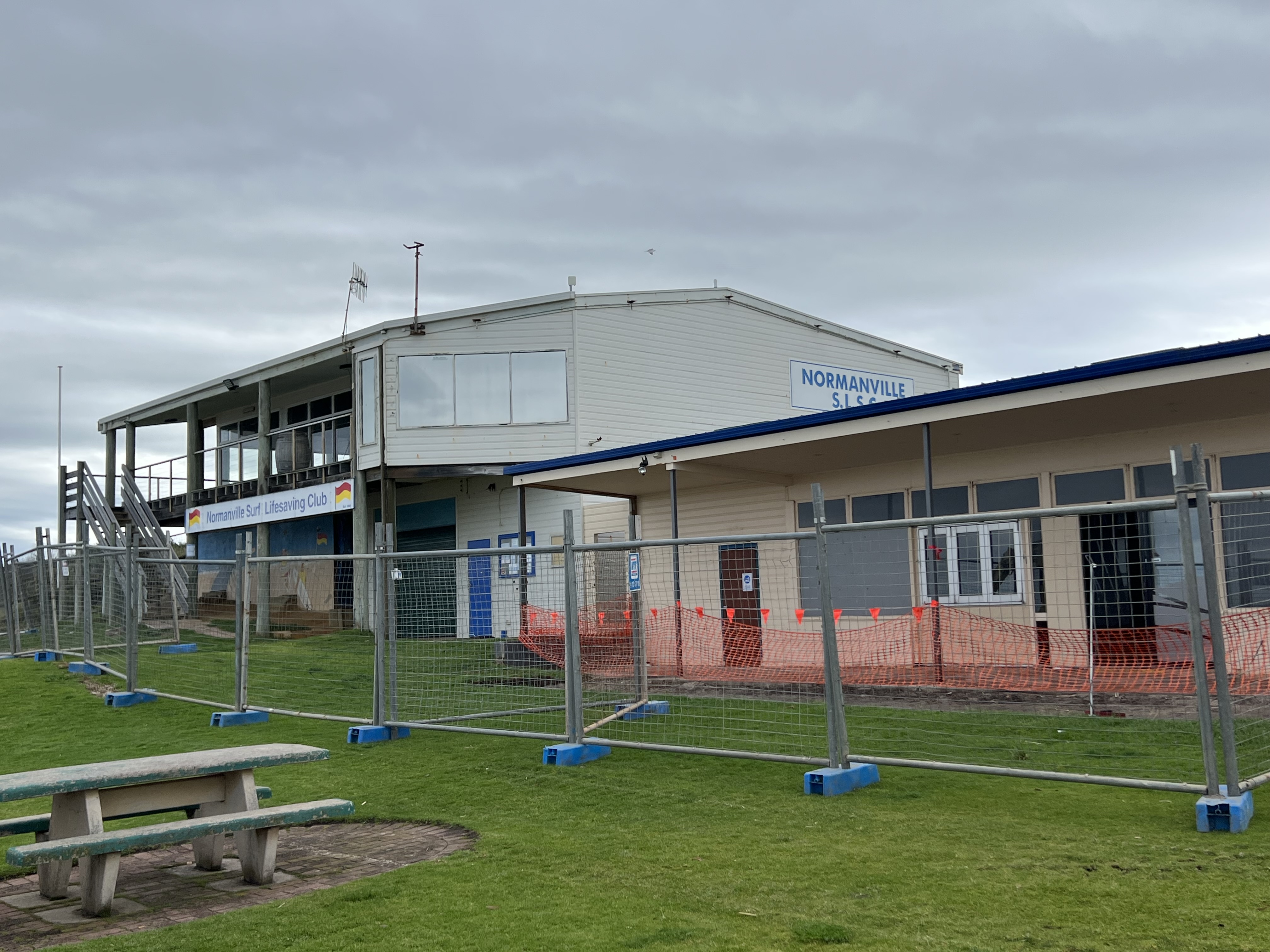 A photo of the old Normanville Surf Life Saving Club and Cafe/Kiosk building, surrounded by construction fencing and bunting