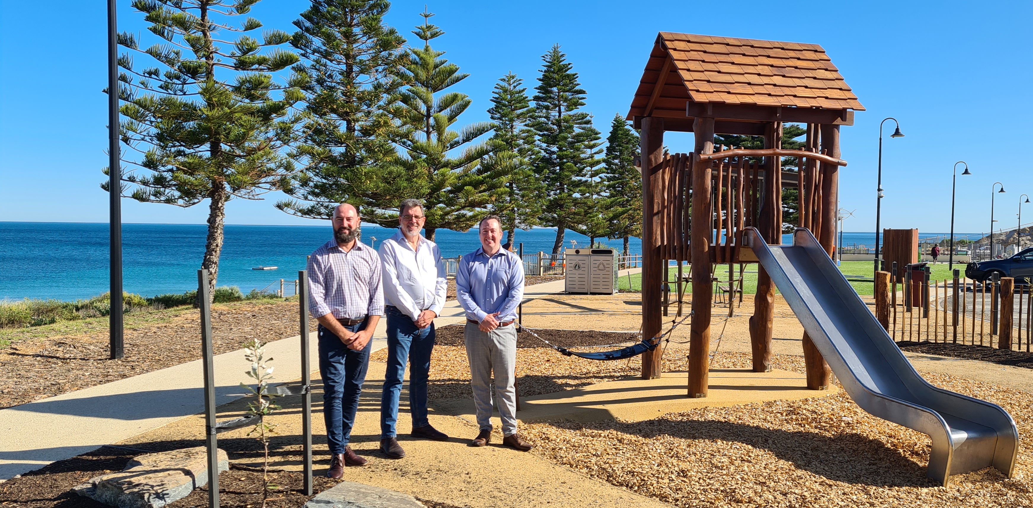 This is an image of Ross Whitfield, Mayor Darryl Houston and CEO Nathan Cunningham are standing in the playground at the Normanville Foreshore with the beach in the background
