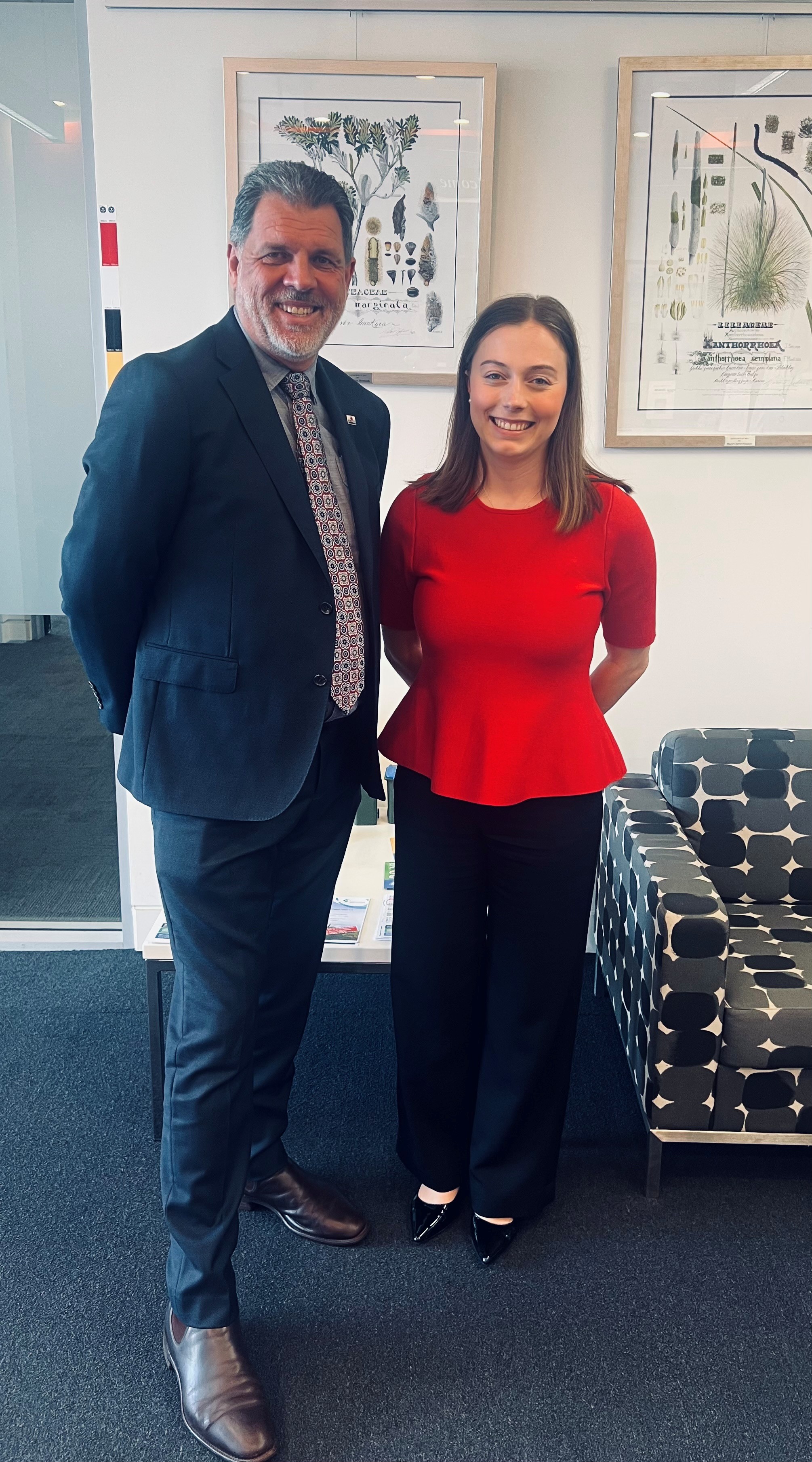 Photograph of Mayor Darrryl Houston and Senator Charlotte Walker standing indoors in a professional setting, with framed botanical prints on a white wall behind them